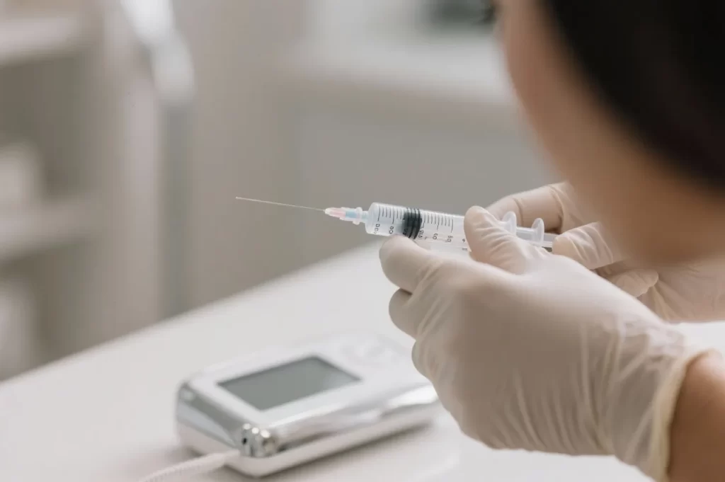 Syringe held by a gloved hand, preparing for weight loss injection, with a digital device in the background, emphasizing physician-supervised medical weight loss.