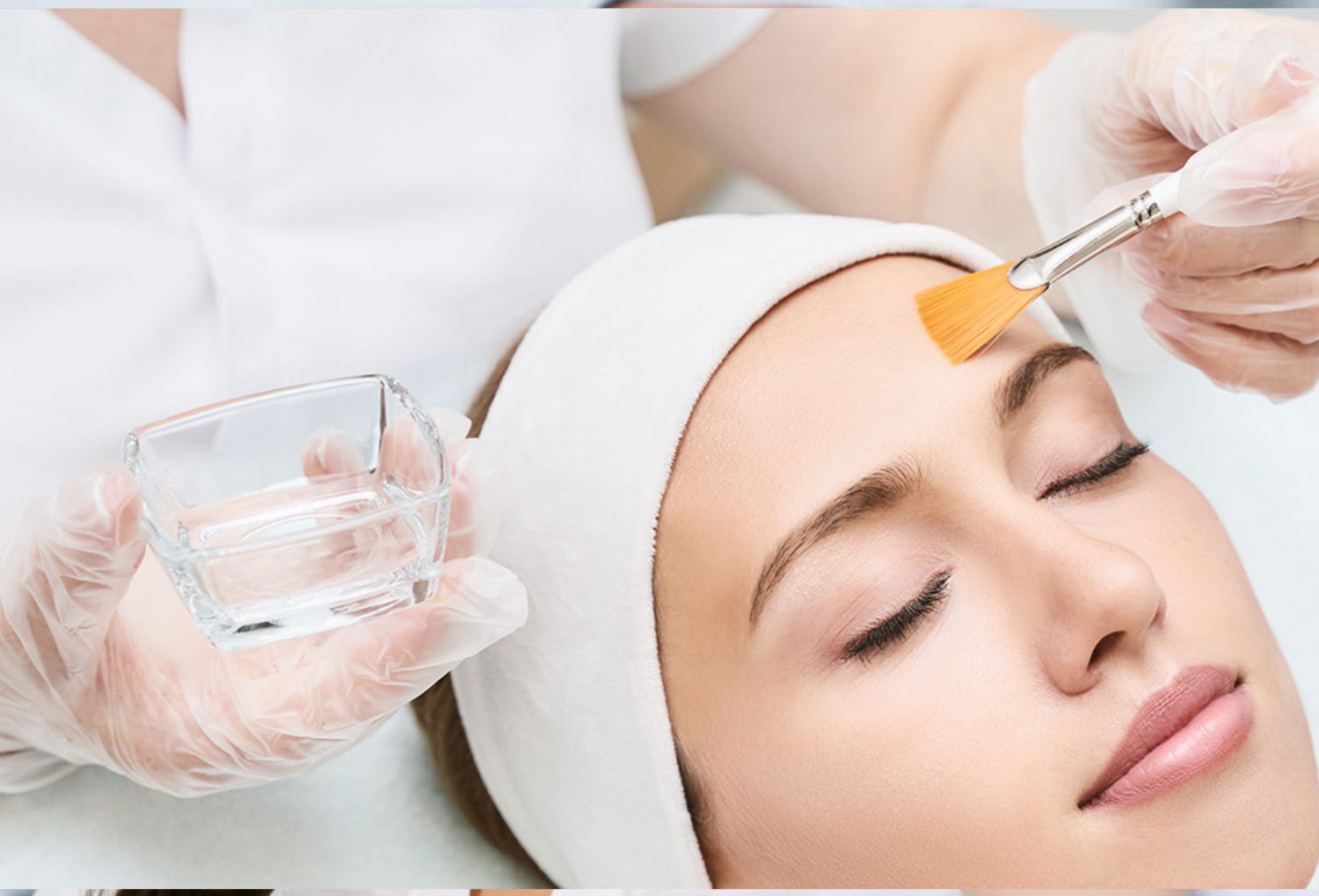 Woman receiving a facial treatment with a brush, while a professional holds a small glass container, emphasizing clinical skincare services at Skin & Body Med Spa.