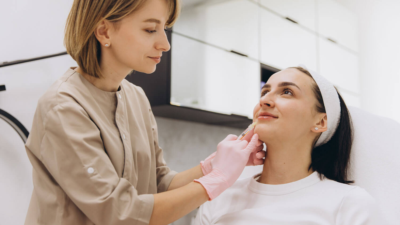 Professional aesthetician administering lip augmentation procedure with syringe to client in a spa setting, highlighting non-surgical cosmetic enhancement at Skin & Body Medical + Wellness Spa.