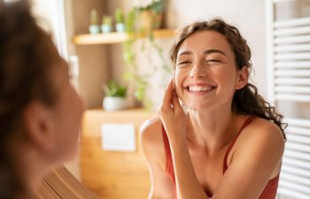Smiling woman applying skincare in a bright, welcoming space, reflecting themes of rejuvenation and wellness related to MedSpa treatments.